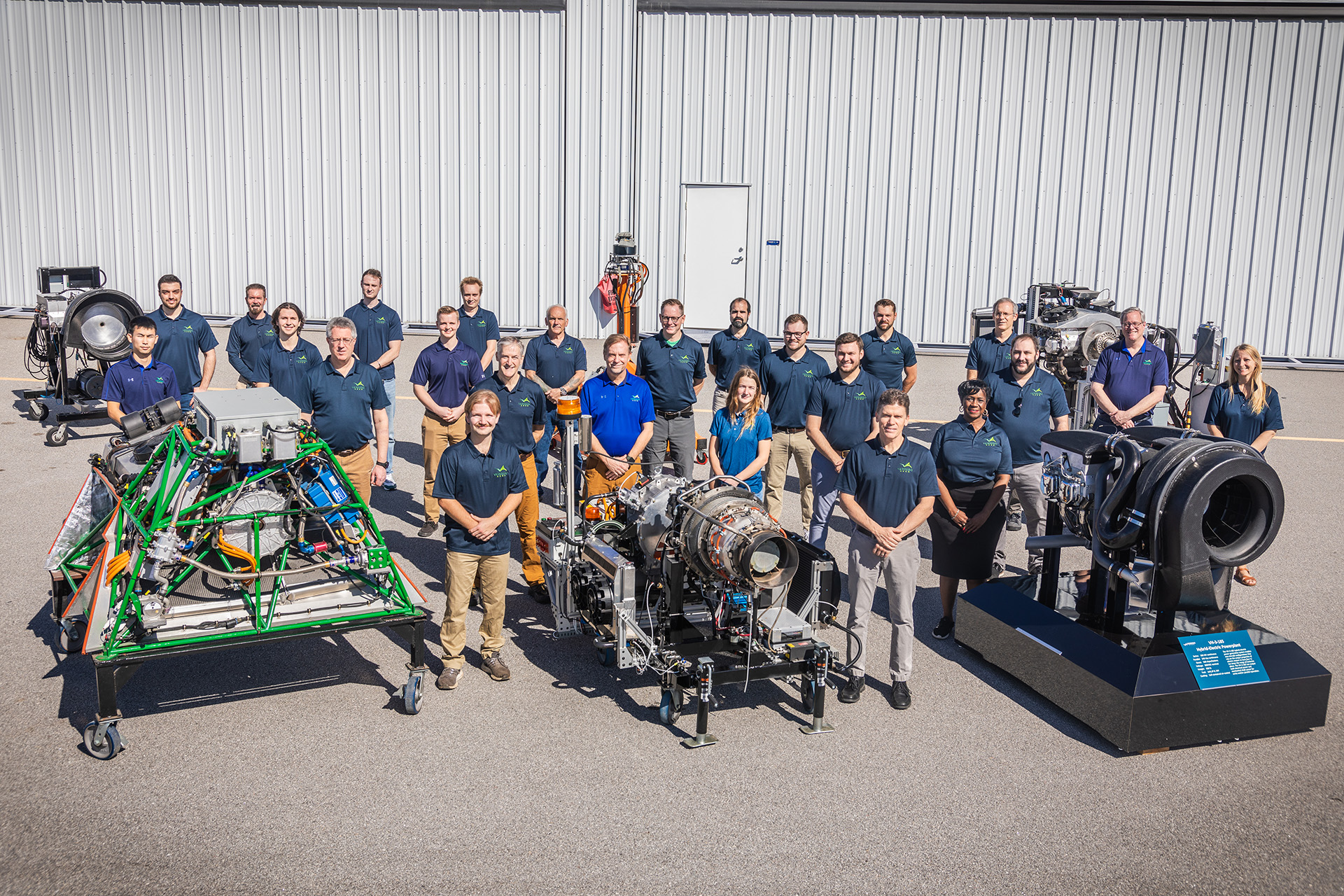 The VerdeGo Aero team standing outdoors among several full-scale hybrid-electric powerplant test articles
