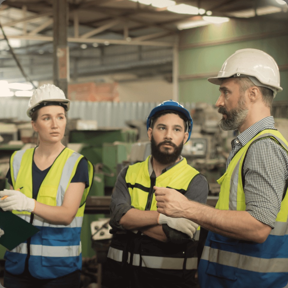Three people in hard hats discussing work on an industrial floor