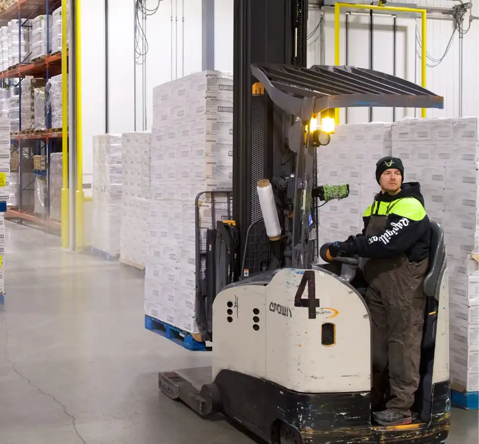 A bundled-up warehouse worker operates a forklift among pallets of boxed products