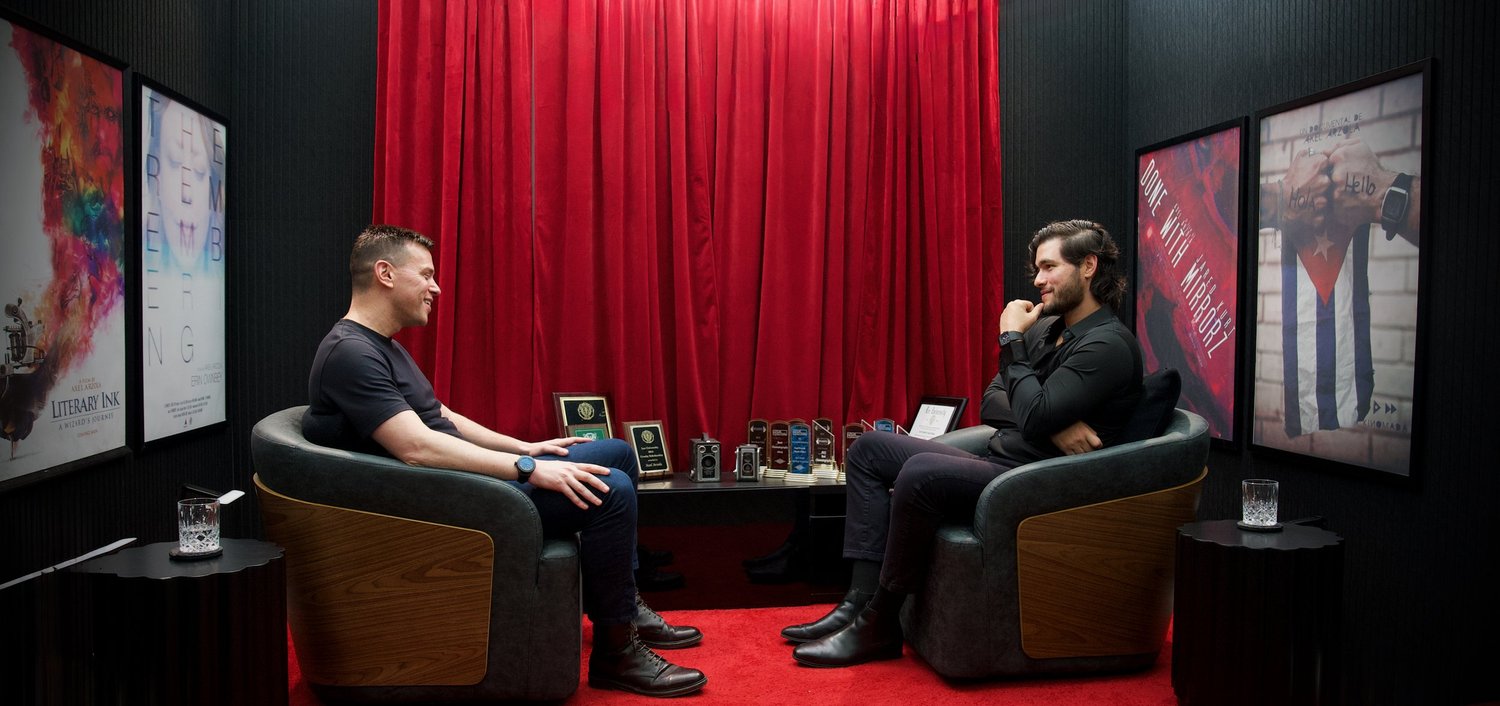 Omri Yoffe, left, in conversation with Axel Axe in a red-curtained interview studio