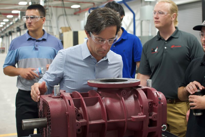 Vicente Reynal in safety glasses inspecting industrial machinery with colleagues during a factory visit