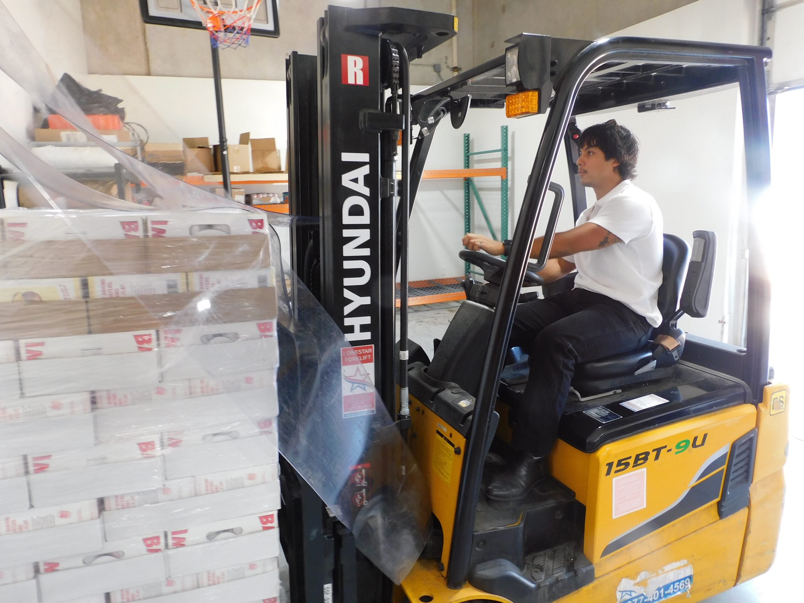 Victor Guardiola operating a forklift beside a pallet of Bawi cans in a warehouse