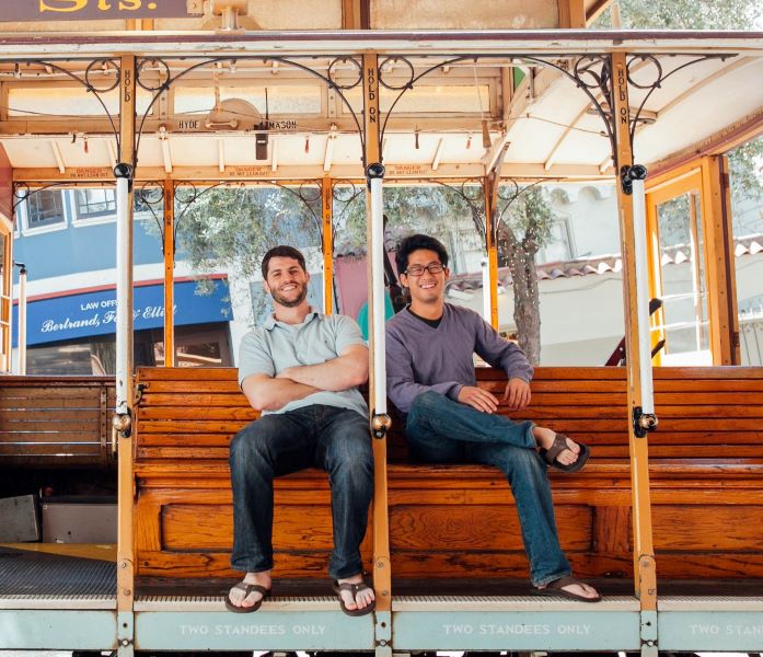 Matt Doka, left, and Victor Ho, right, sitting on a San Francisco cable car
