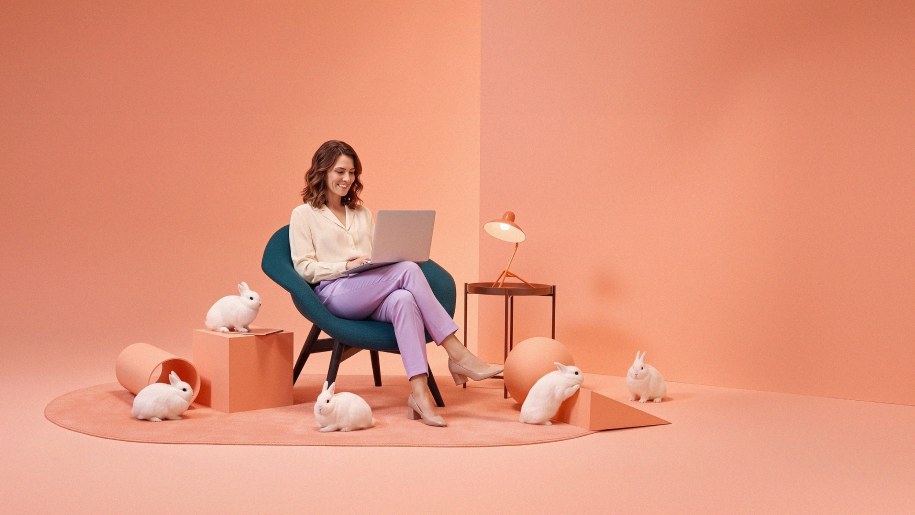 A woman working calmly on a laptop in a styled orange set surrounded by white rabbits