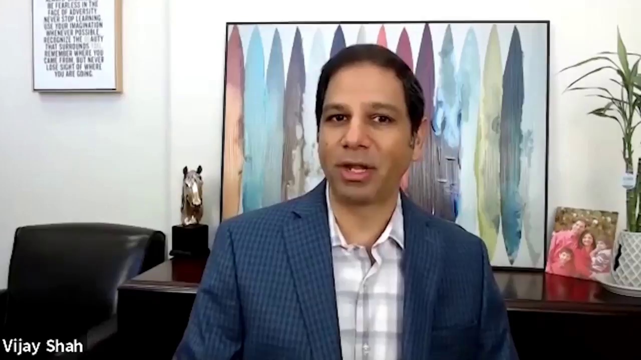 Vijay Shah speaking in a V2Solutions founder interview, seated in front of colorful artwork