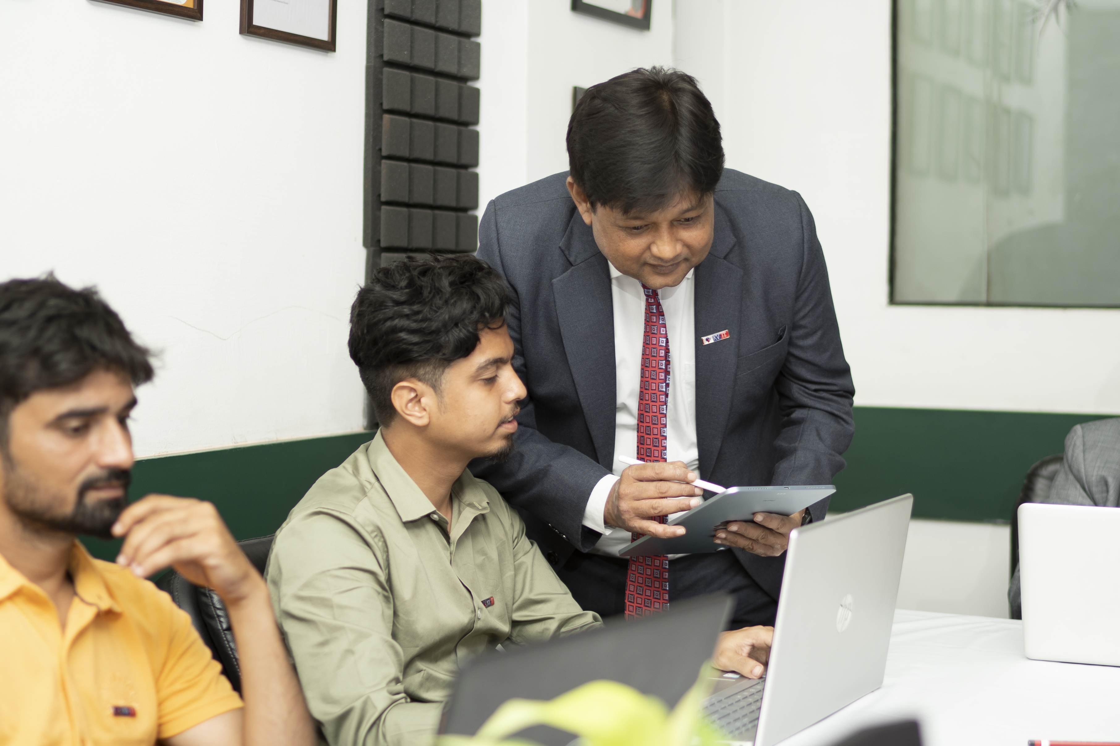 Vikas Debnath leaning over a tablet beside learners working at laptops