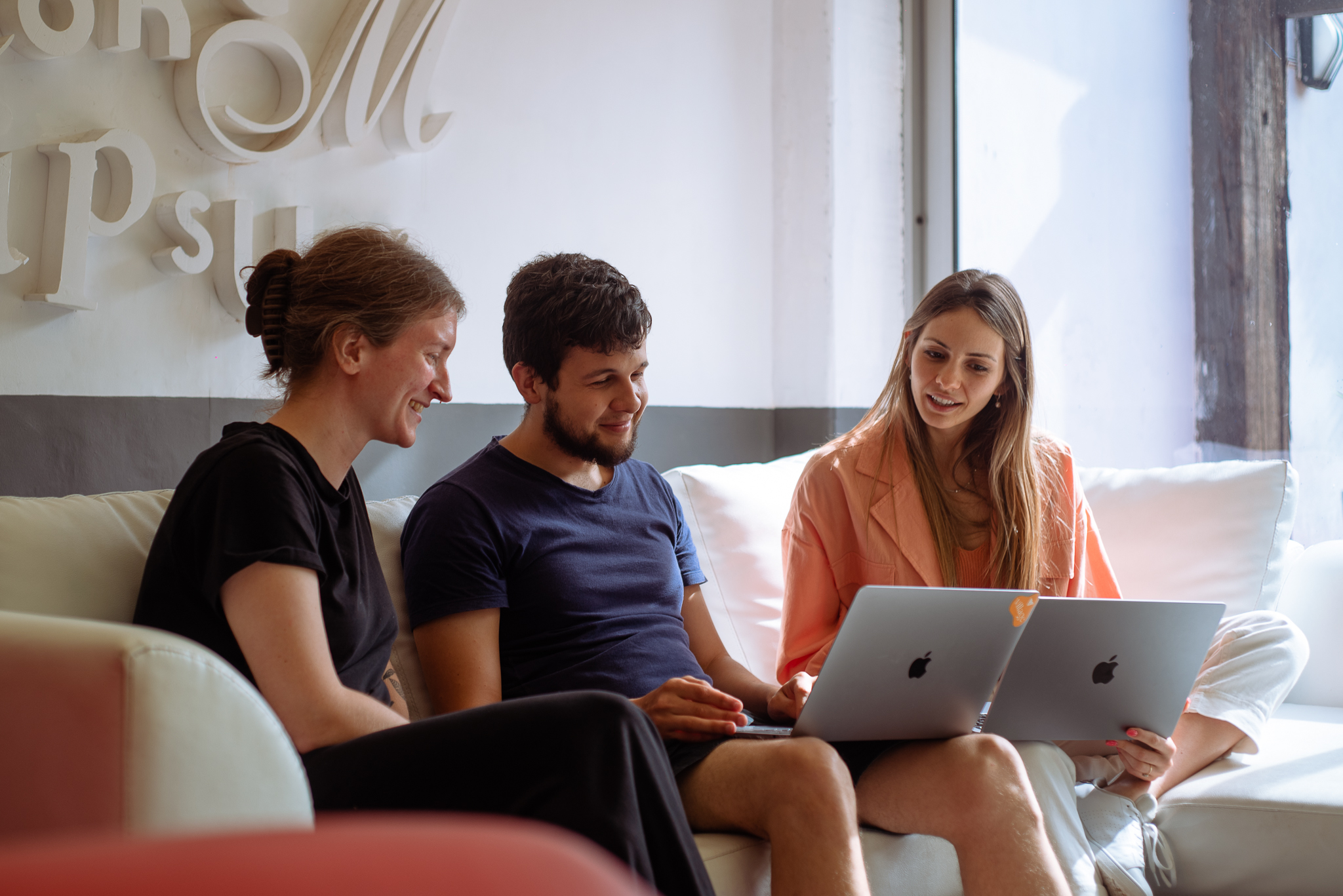 Three members of the Village team working together with laptops on a sofa