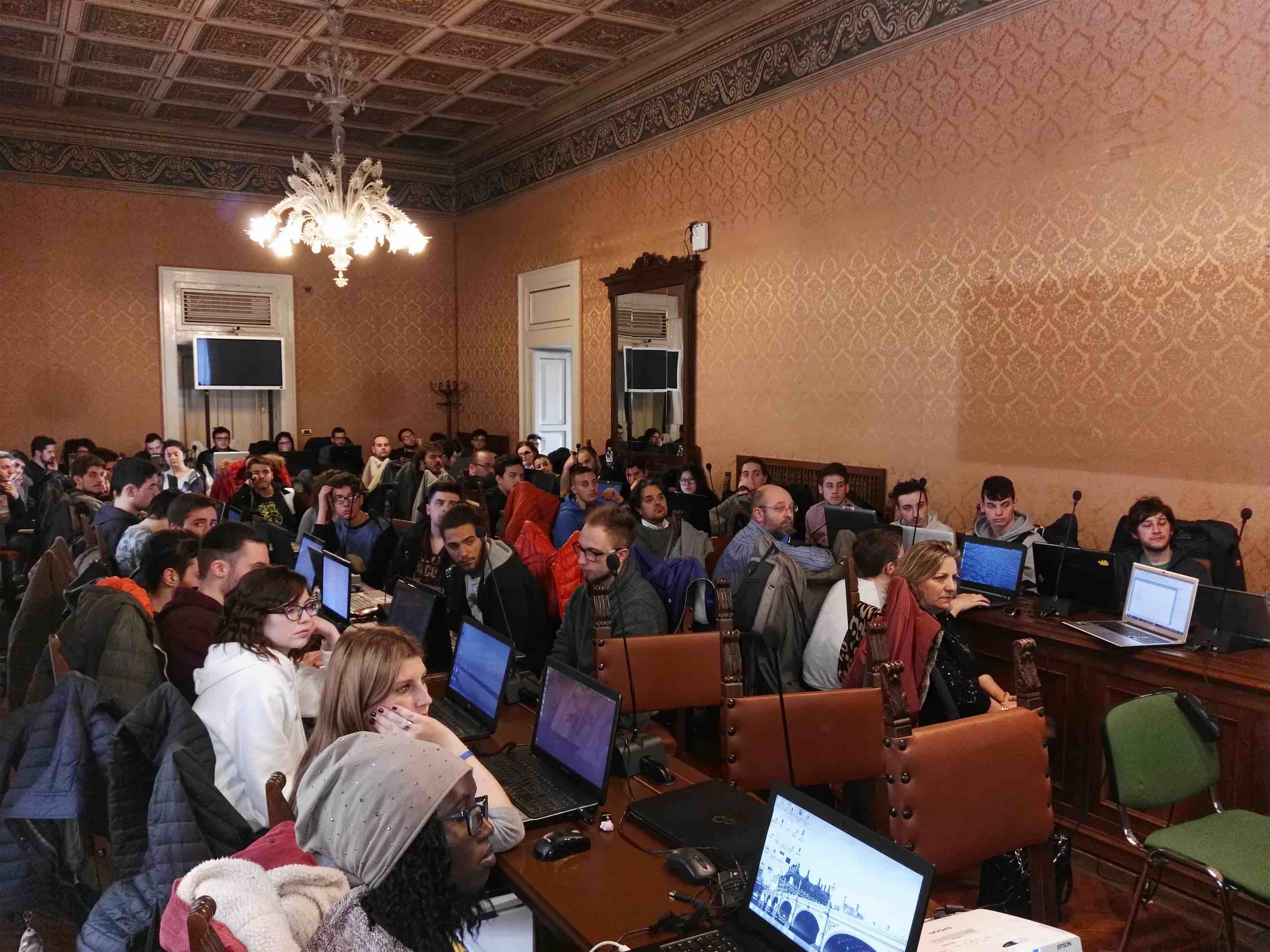 Students and participants working on laptops in an ornate classroom, photographed on the cogita website