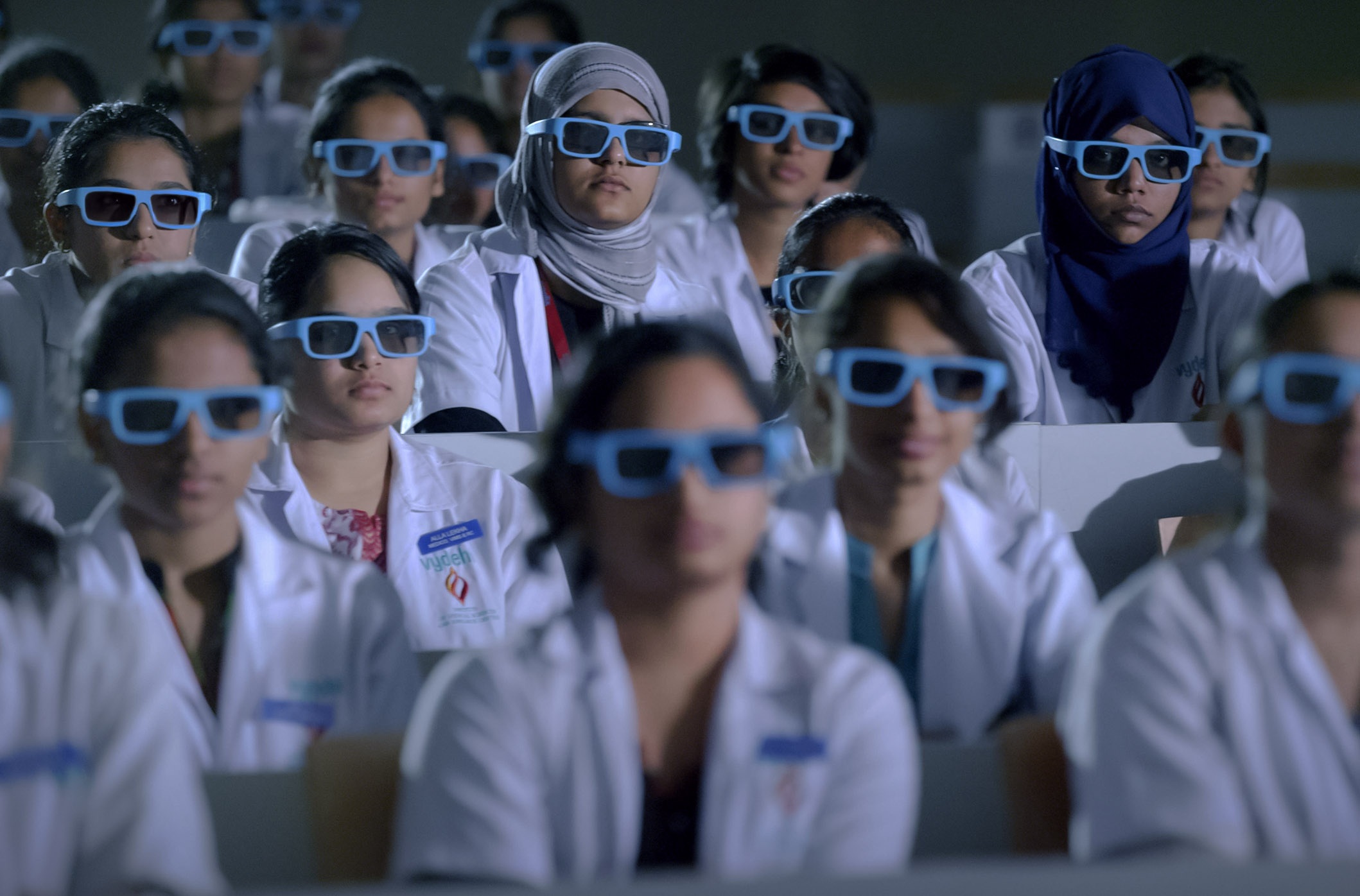 Students in white coats watching a lesson through blue stereoscopic glasses