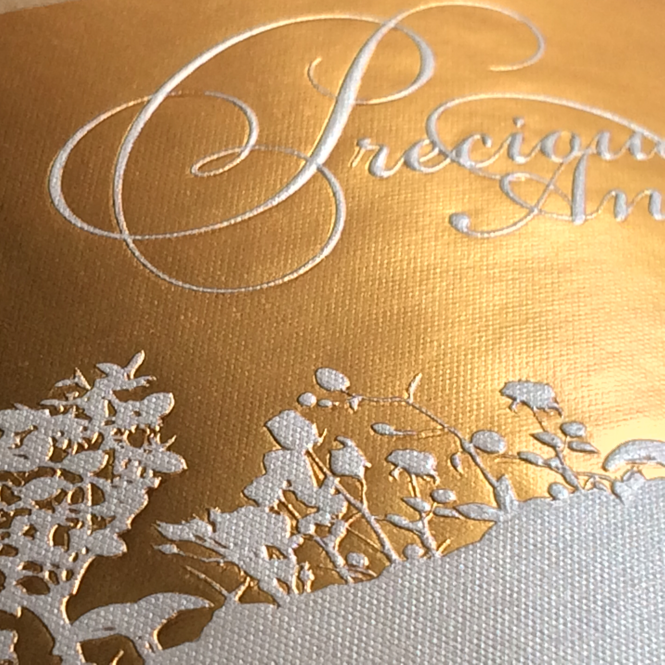 Close-up of a gold-toned Vintage 99 label sample with script lettering and a textured floral pattern