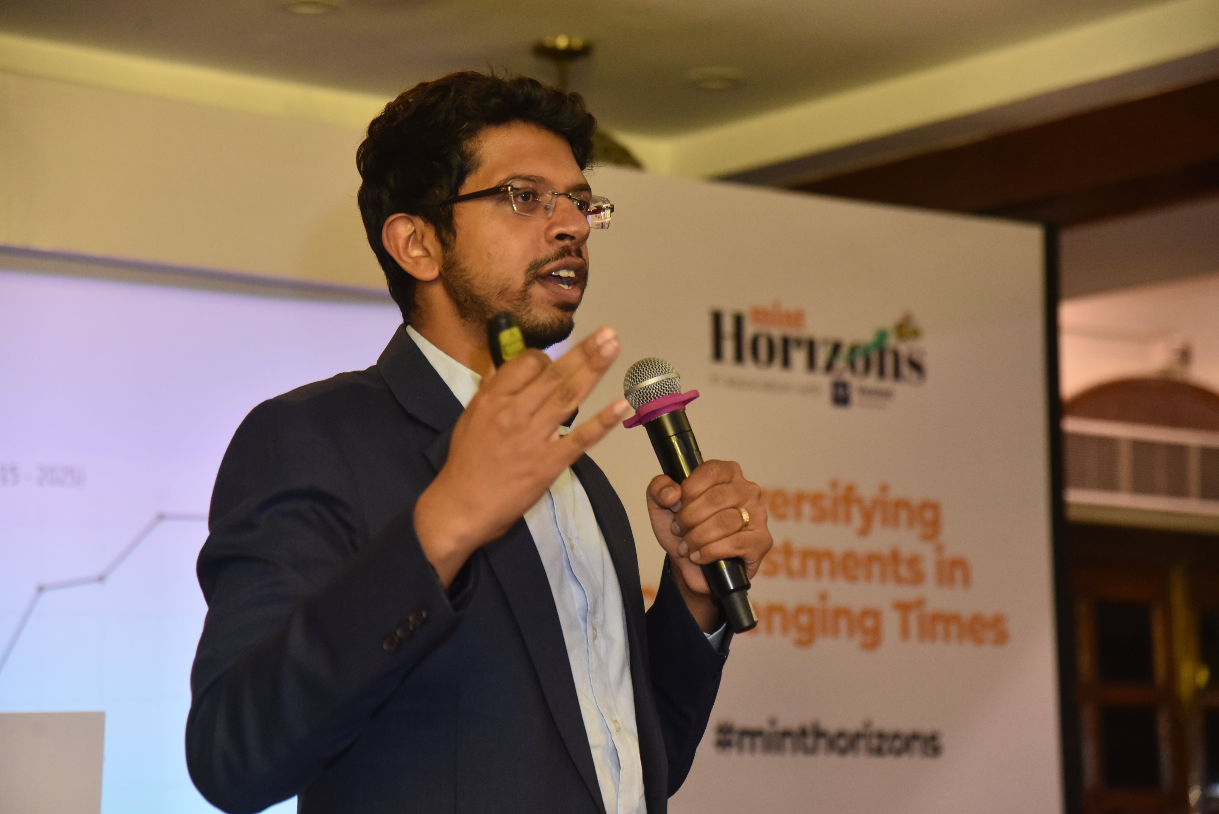 Viram Shah speaking into a microphone at the Mint Horizons conference, with a screen about diversifying investments behind him
