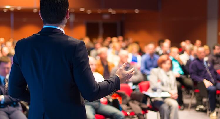 A presenter speaking to a seated business audience