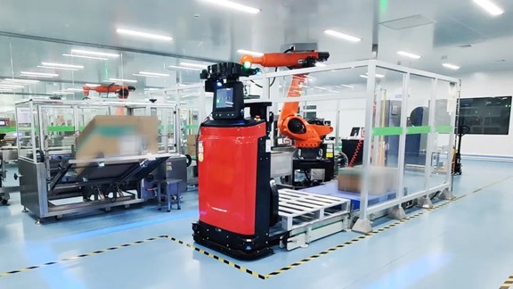 Red VisionNav autonomous forklift beside conveyors and industrial robot arms in a pharmaceutical facility