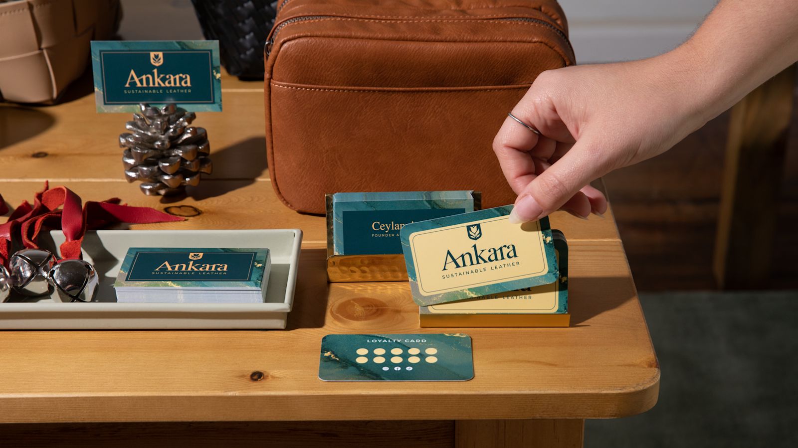 A hand lifts an Ankara business card beside a leather bag and matching loyalty cards