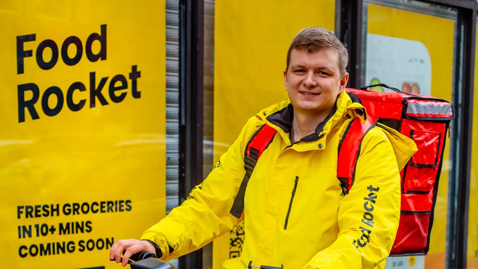 Vitaly Alexandrov wearing Food Rocket delivery gear outside a storefront with the company’s yellow branding