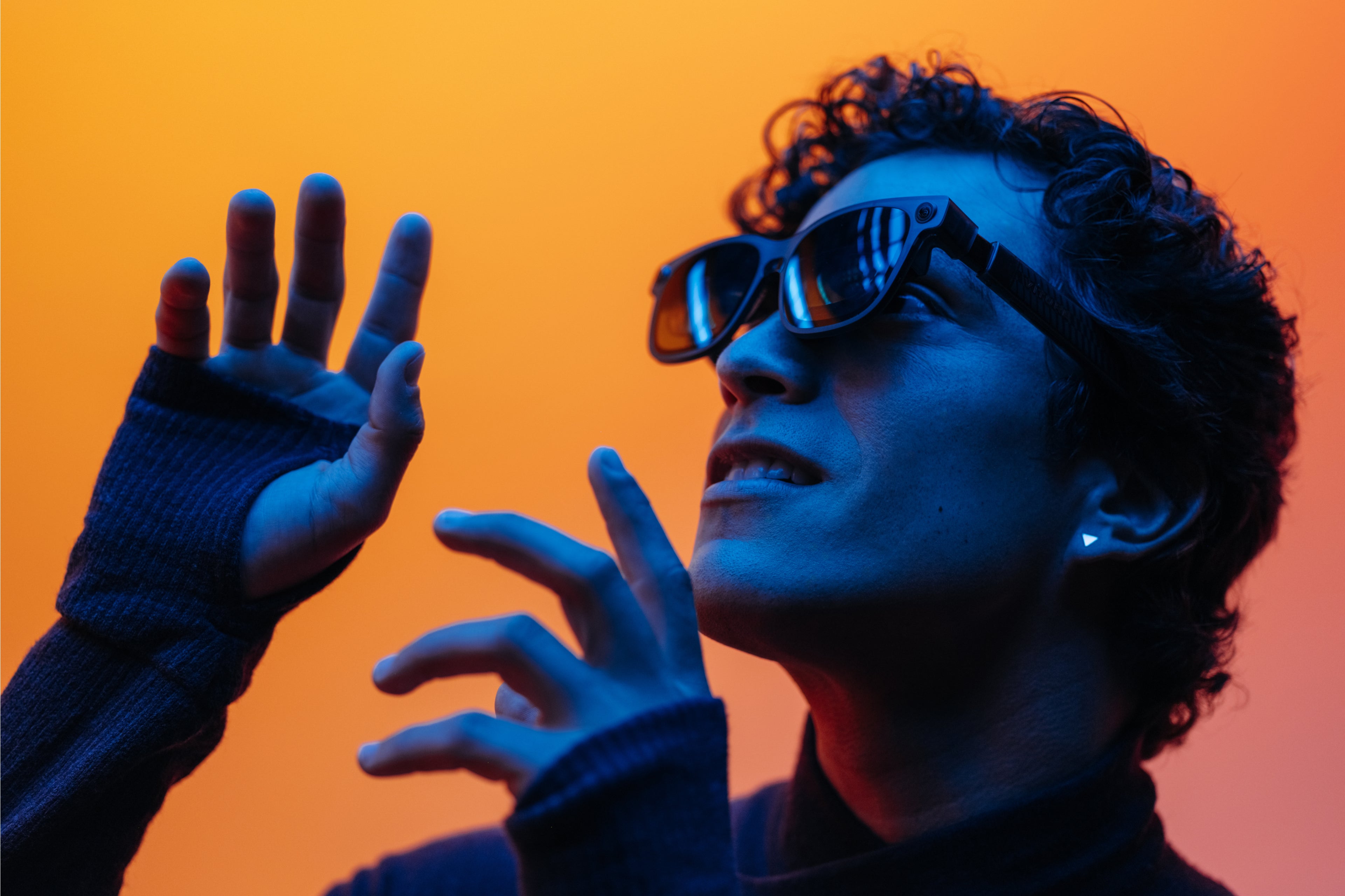A person wearing VITURE Luma Ultra glasses and raising both hands against orange and blue studio lighting