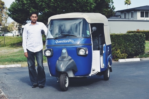 Vivek Bhaskaran standing beside a blue QuestionPro auto-rickshaw