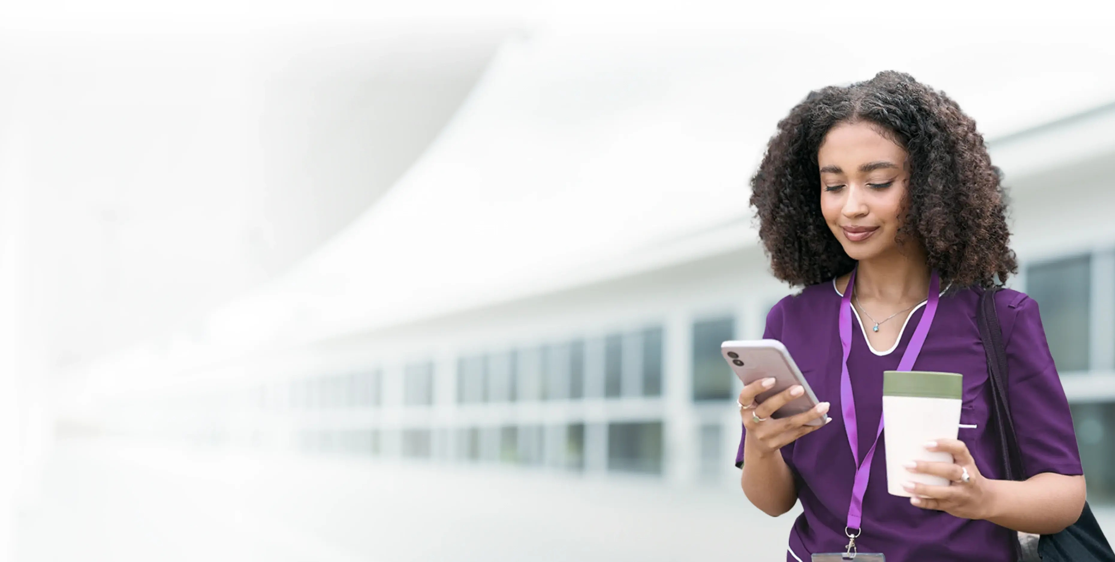 A healthcare worker in purple scrubs checking her phone in a bright hallway