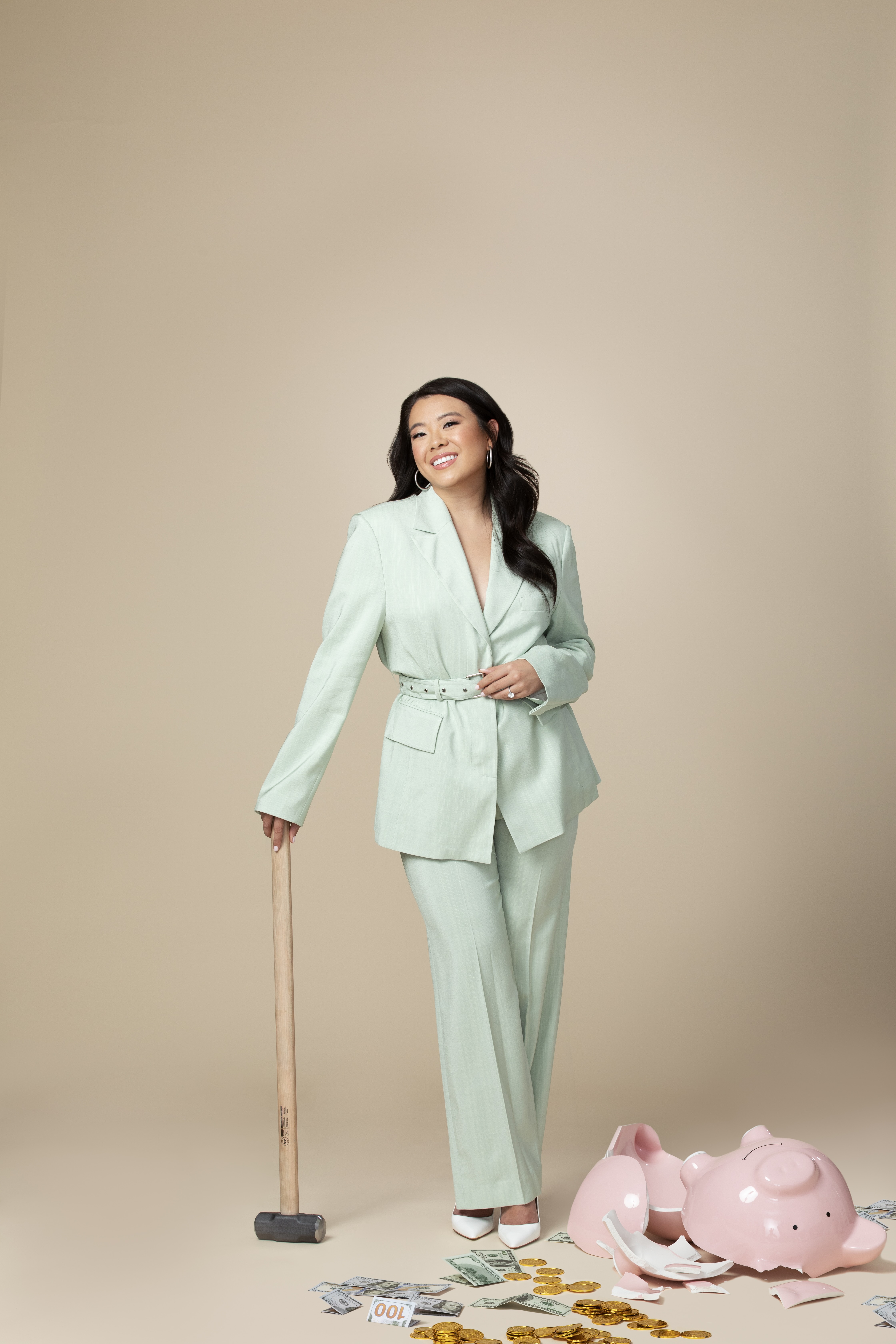 Vivian Tu in a mint green suit standing beside a broken pink piggy bank