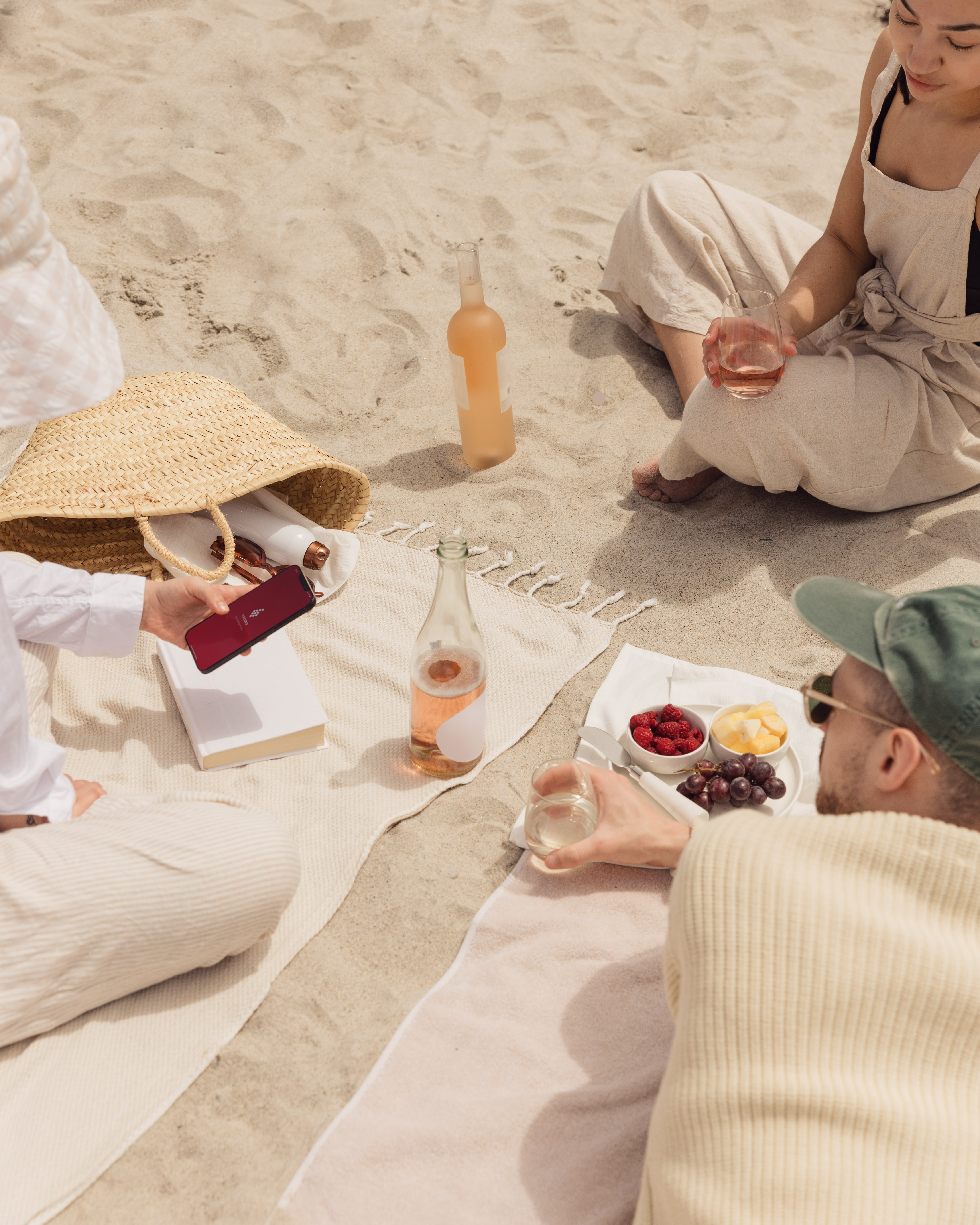 Friends sharing rosé on a beach while one holds a phone displaying Vivino