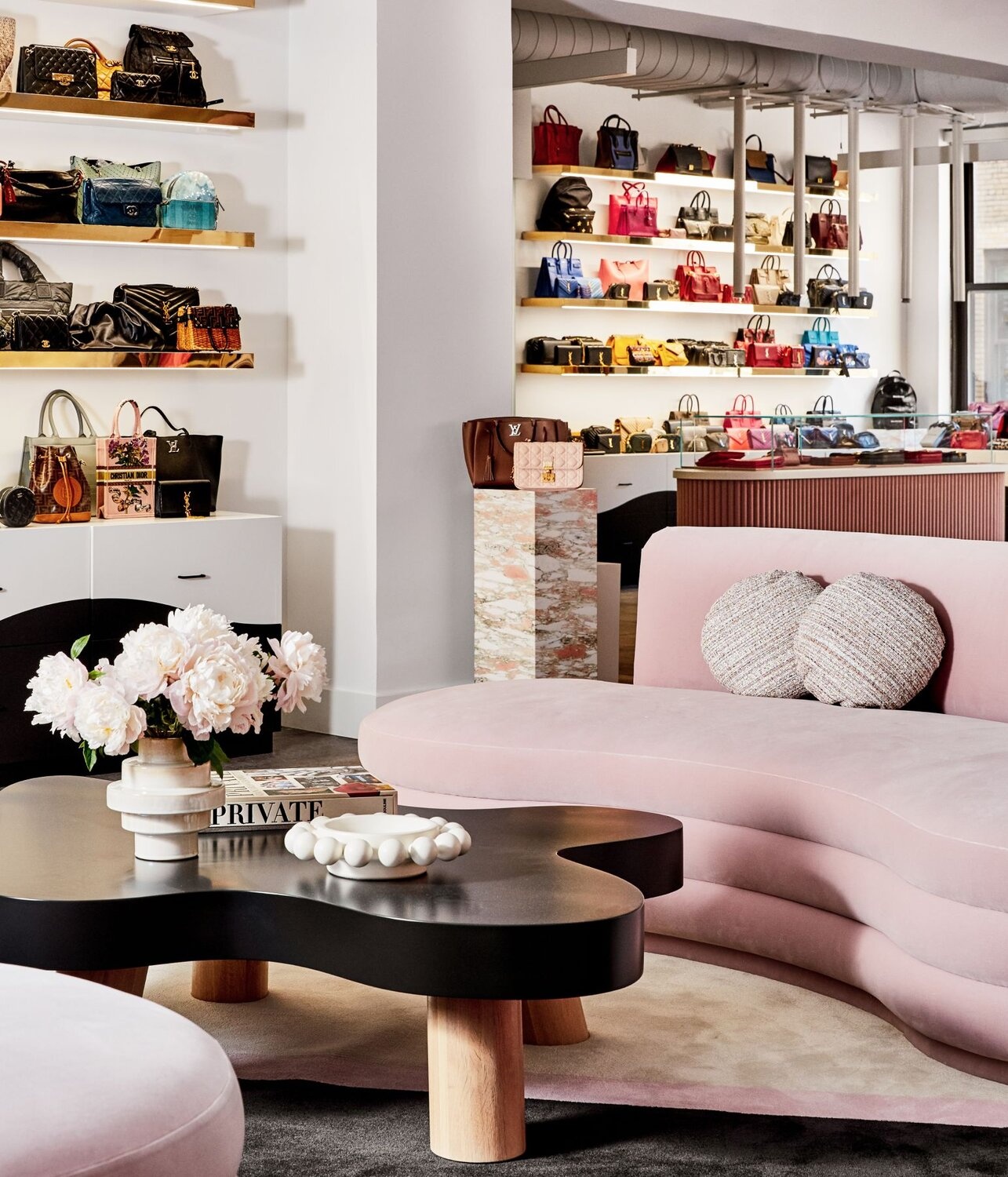 Designer handbags on shelves surrounding pink seating in Vivrelle’s New York showroom