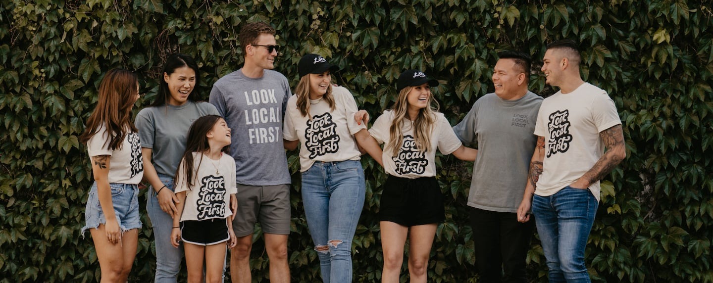 A group wearing Look Local First shirts gathers in front of a leafy wall