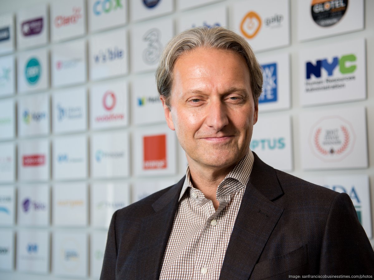Vlocity co-founder David Schmaier standing before a wall of company logos