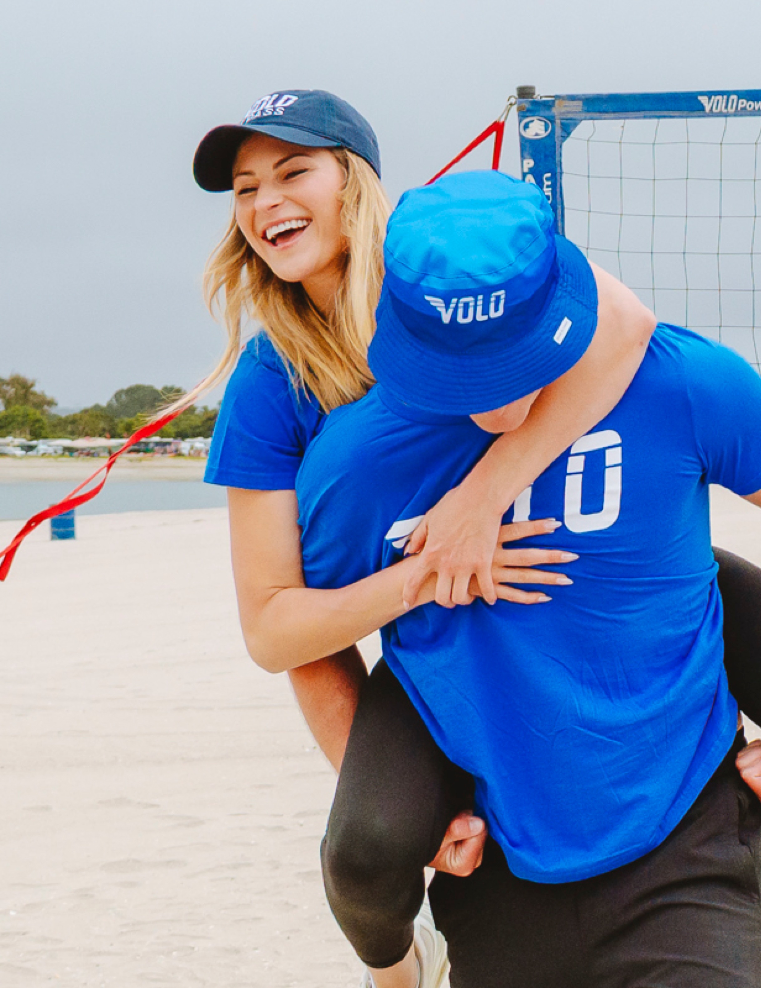 Two Volo players laughing beside a volleyball net