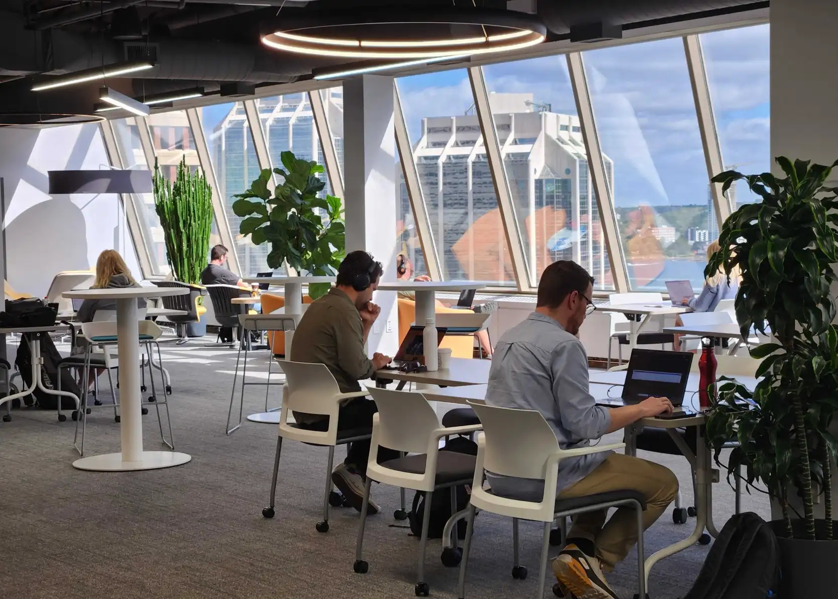 People working on laptops beside the large windows and plants in Volta’s Halifax workspace