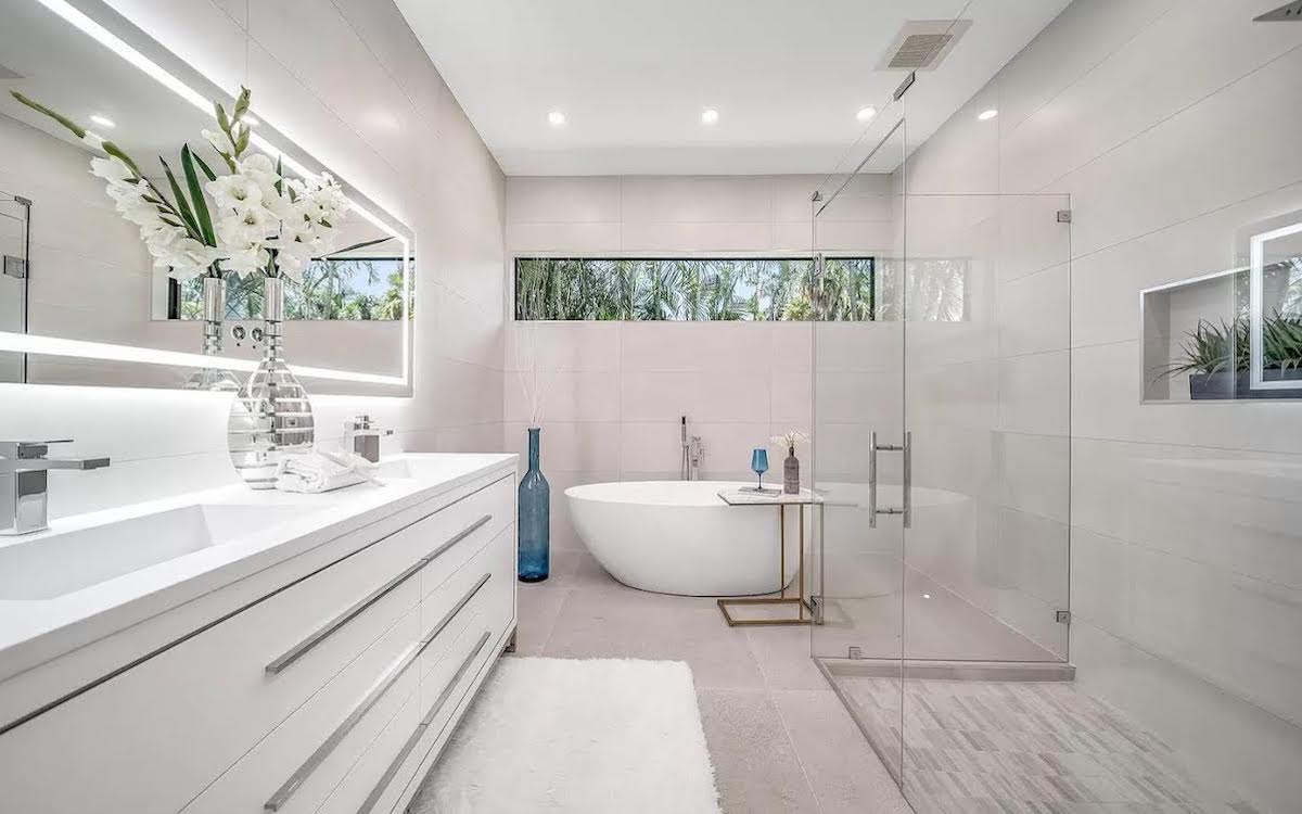 Bathroom Place bathroom setting with white vanity, illuminated mirrors, bathtub, and glass shower