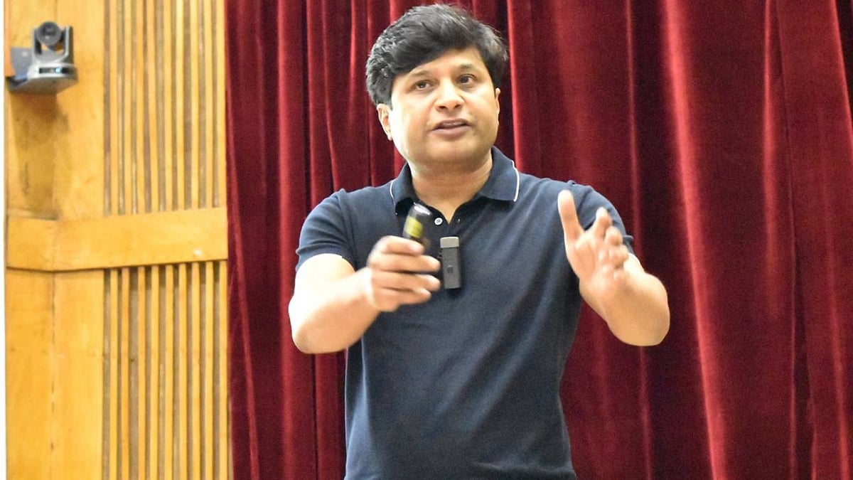 V. S. S. Mani speaking with a presentation clicker in front of red curtains