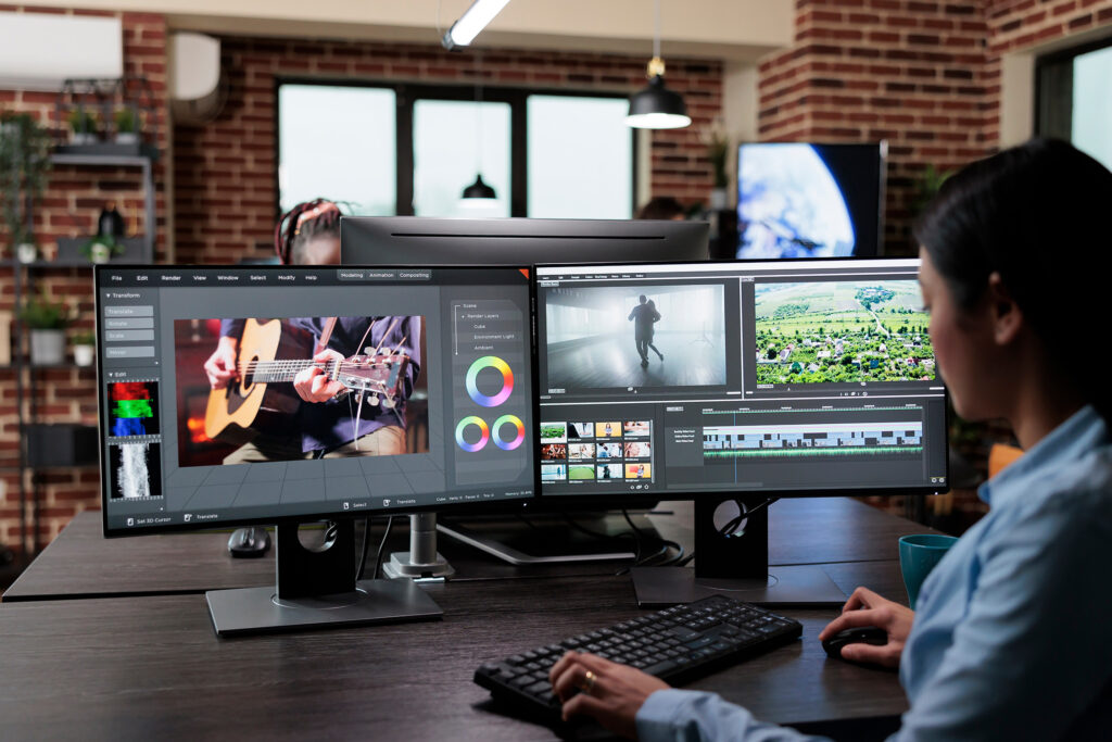 An editor working across multiple monitors, including color grading controls and a video timeline