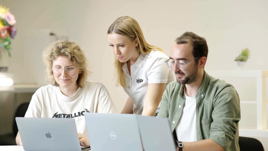Three colleagues gathered around laptops in an image from Vypr’s Hallmark work