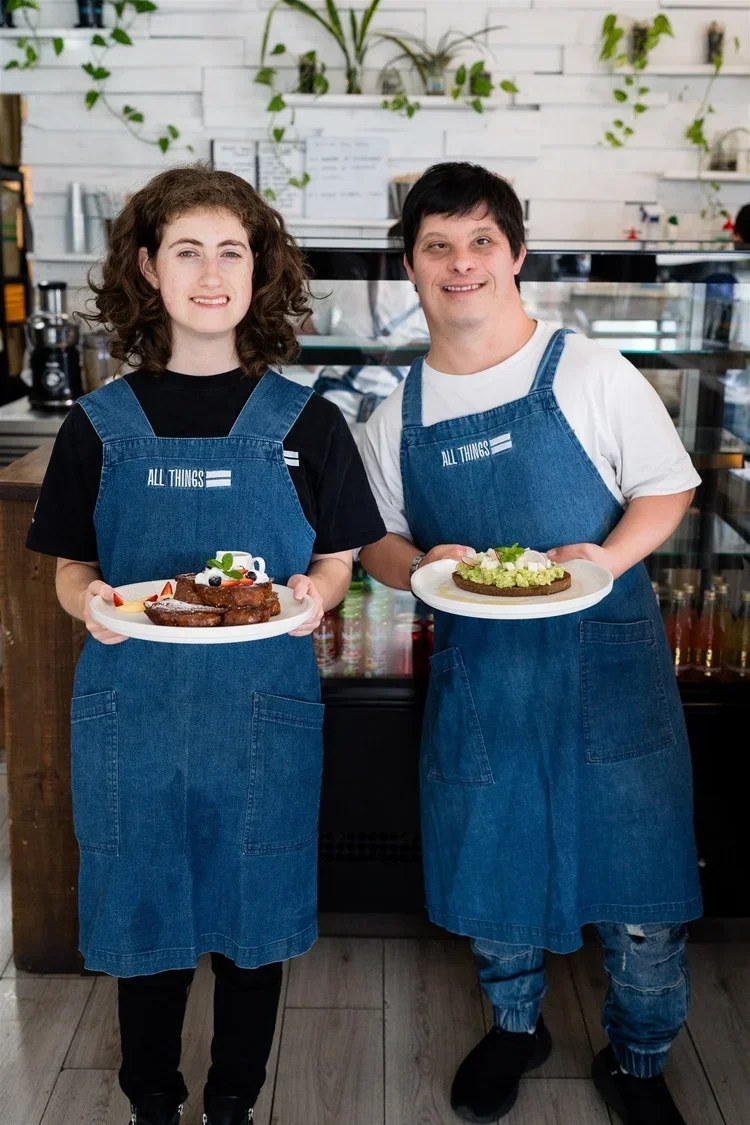 Two neurodivergent hospitality workers holding plates in a cafe