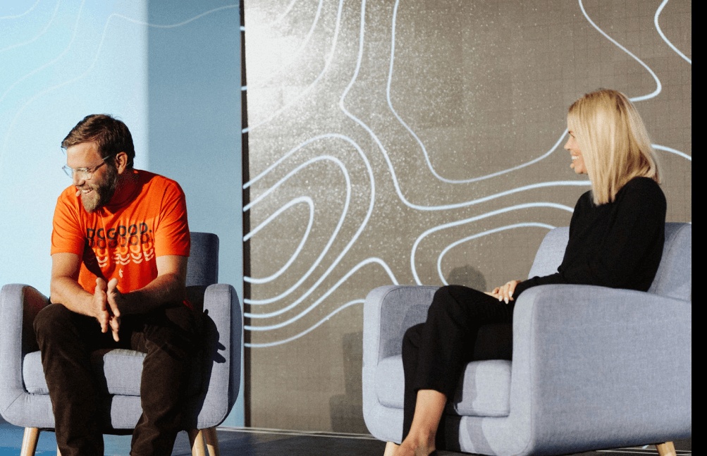 Wade Arnold in an orange Moov shirt speaking with Kara Parkey onstage at the 2022 Money Experience Summit