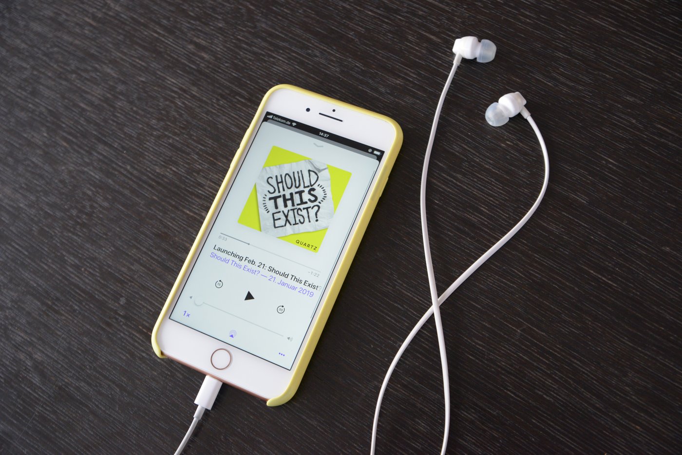 A phone showing the Should This Exist? podcast beside wired earphones