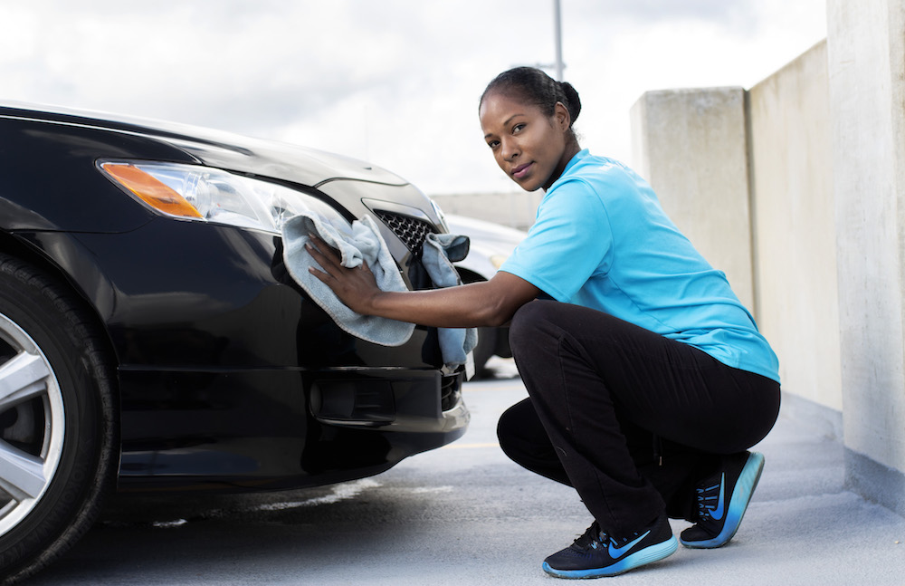 A NuWash technician cleaning the front of a parked car