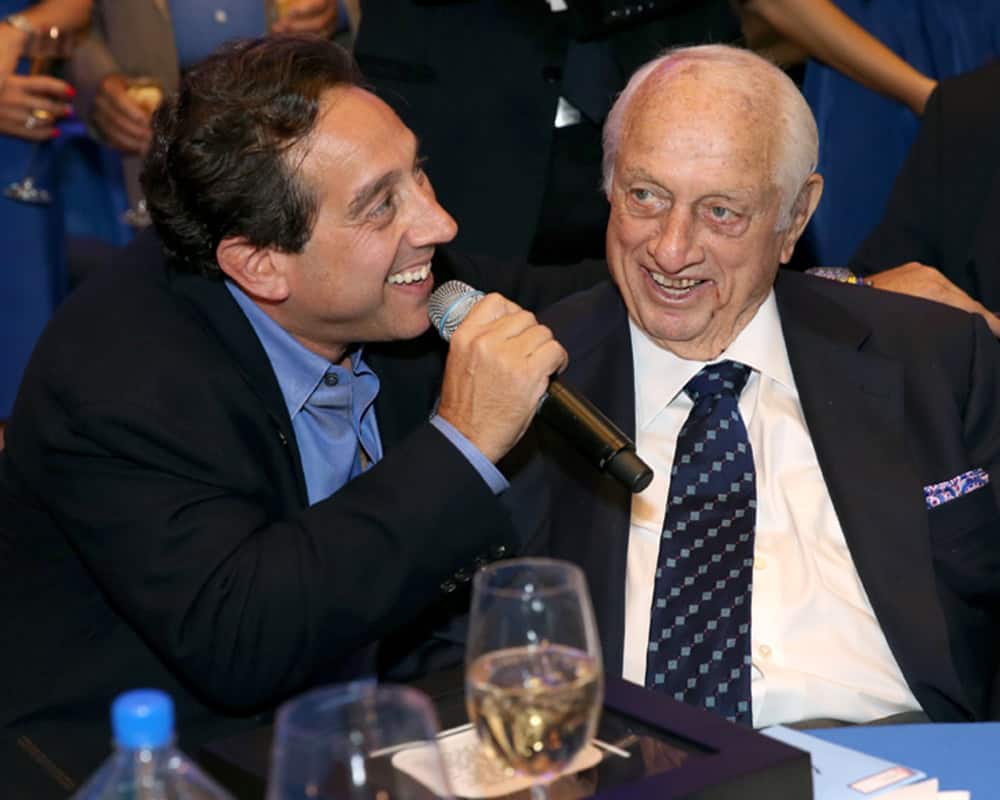 Warren Lichtenstein, left, speaking into a microphone beside a smiling Tommy Lasorda