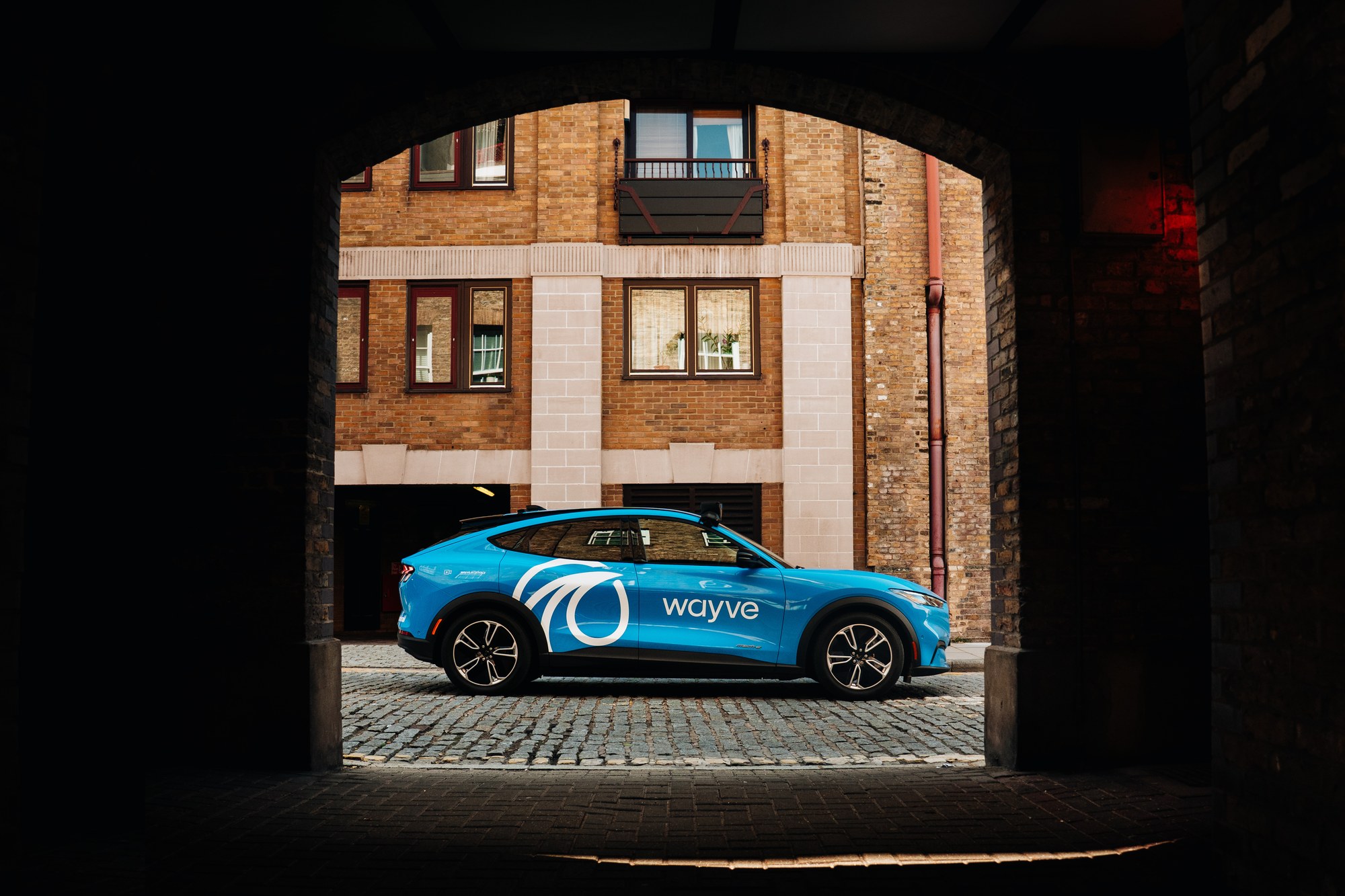 A blue Wayve test vehicle parked beneath an arch in London