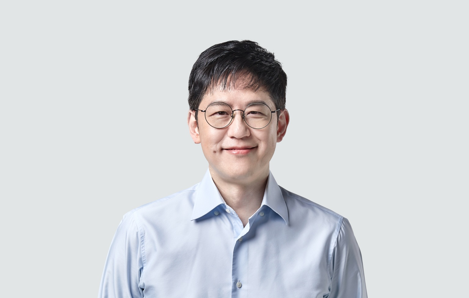 WEBTOON founder Junkoo Kim wearing round glasses and a pale blue shirt