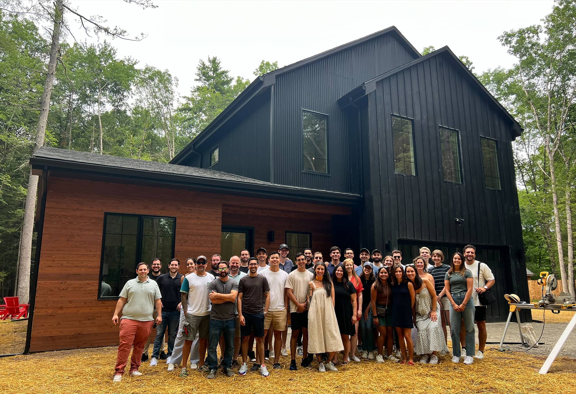 Welcome team gathered outside a dark-clad house surrounded by trees