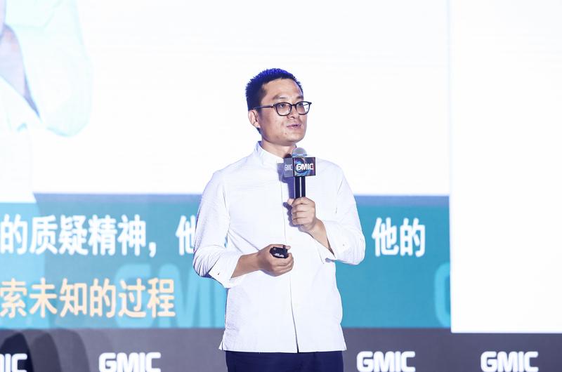 Wen Chu speaking on stage at GMIC with a microphone and presentation remote
