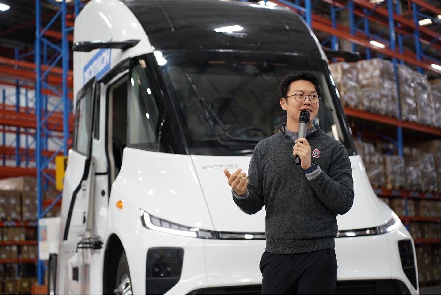 Wen Han holds a microphone in front of a Windrose truck inside a warehouse.