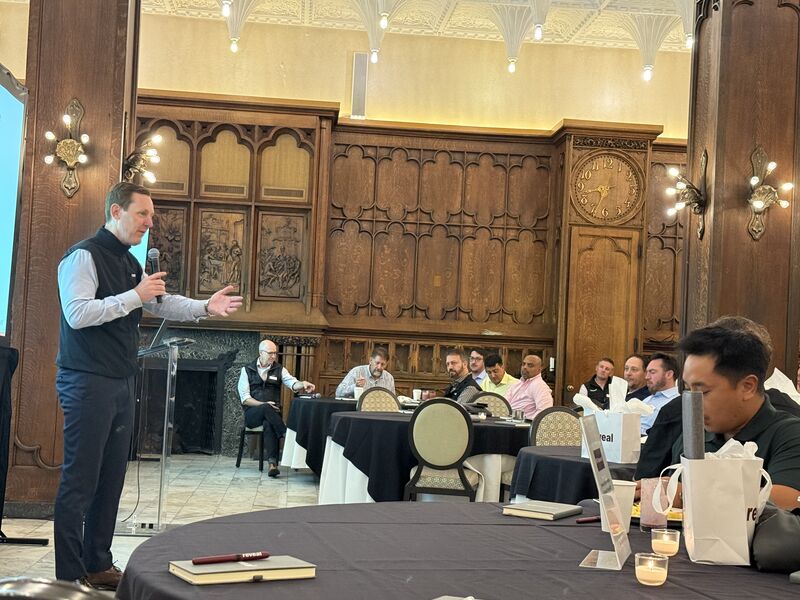 Wendell Jisa speaking into a microphone to seated attendees at Reveal’s Partner Summit, in an ornate wood-paneled room.