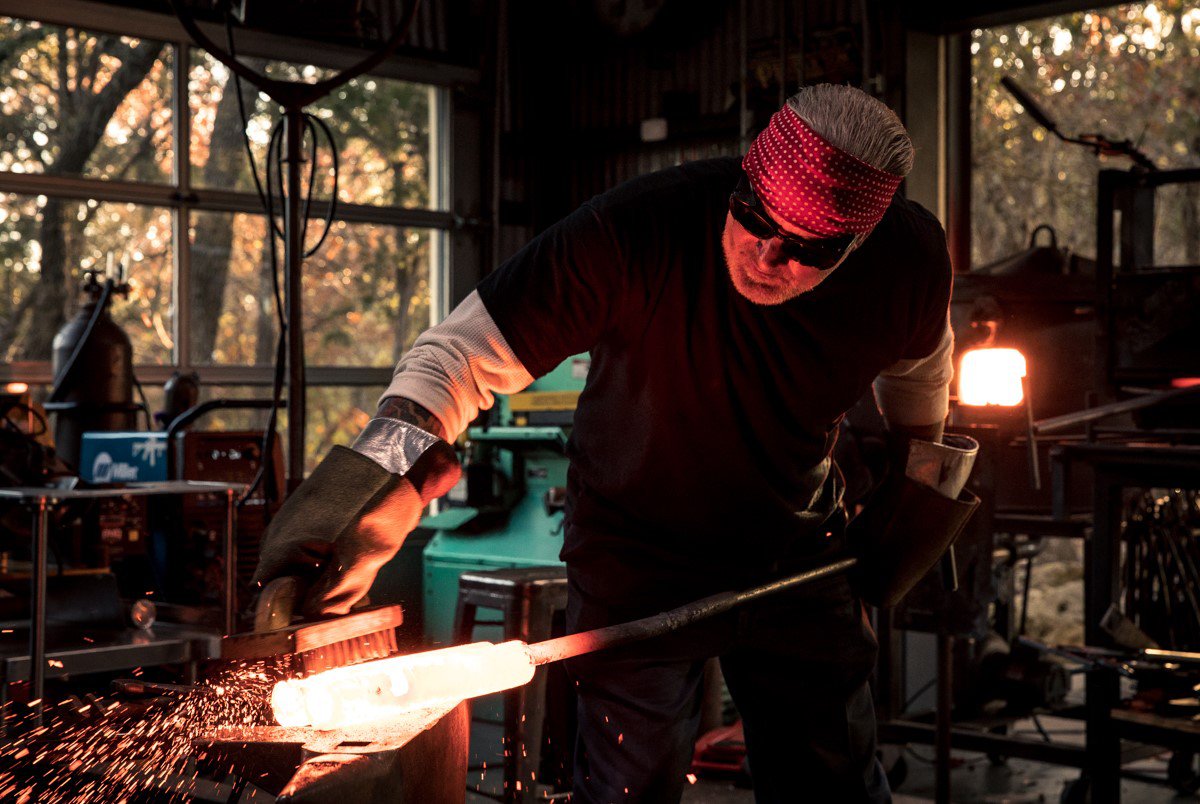 Jesse James brushing a glowing piece of metal in a workshop