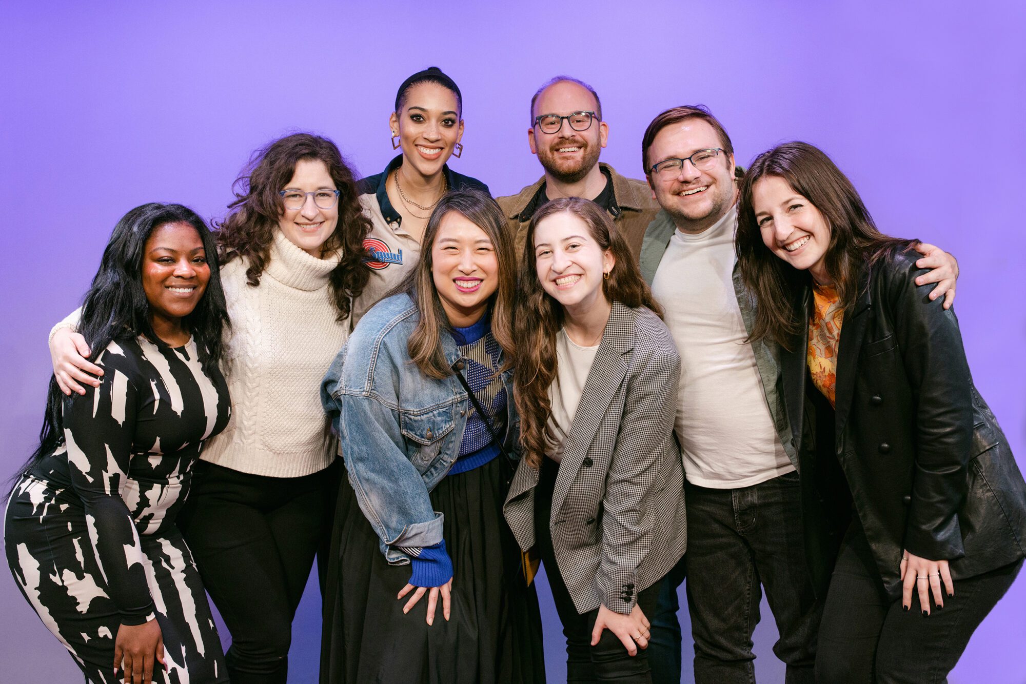 Members of West Wing Writers smiling together at a SpeakEasy event against a purple background