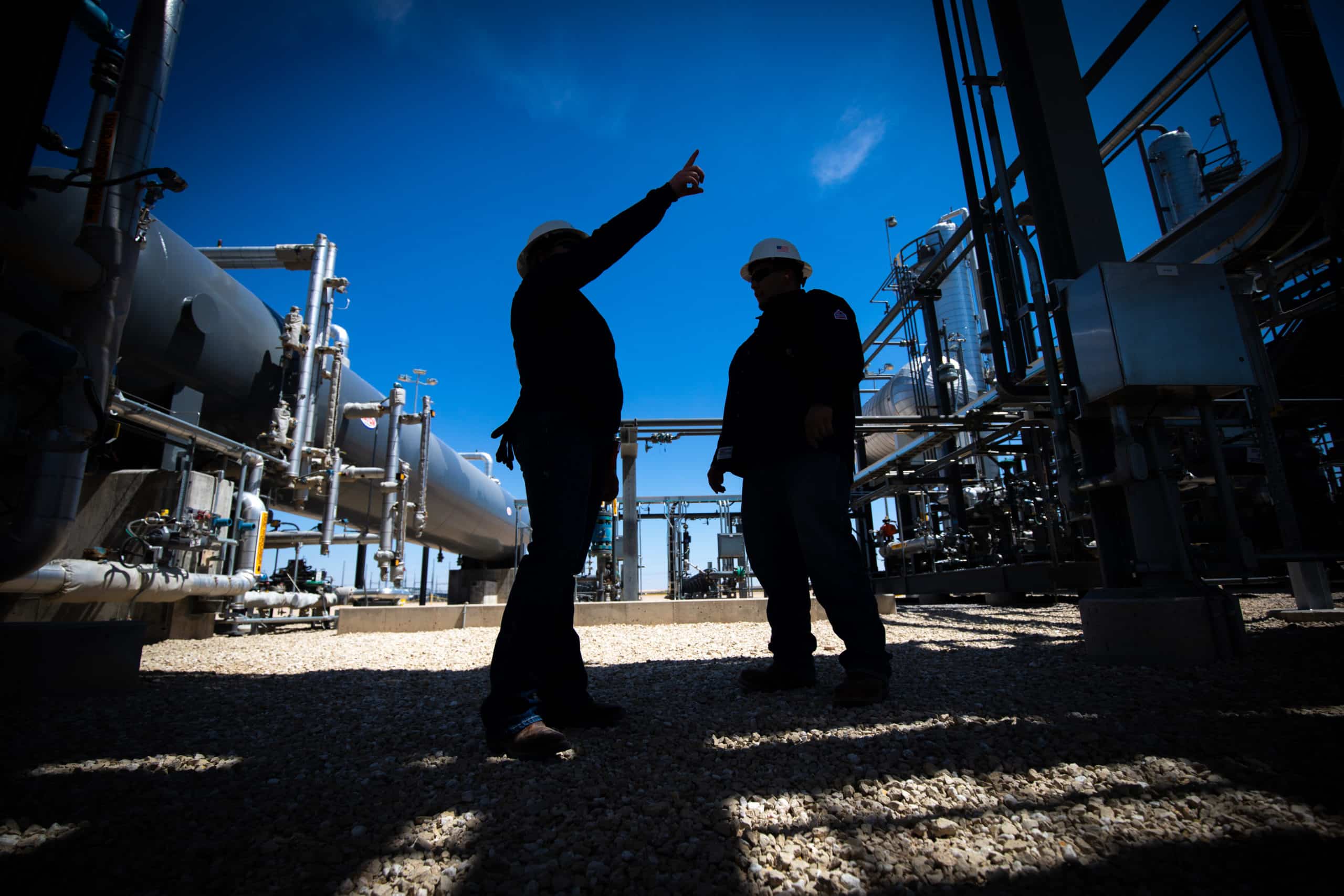 Two hard-hat workers among pipes and processing equipment at Western Midstream’s Mentone facility