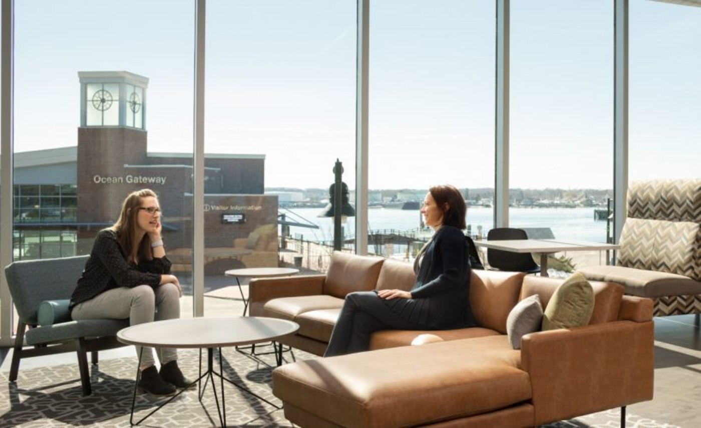 Two people talking beside harbor-facing windows in WEX’s Portland headquarters
