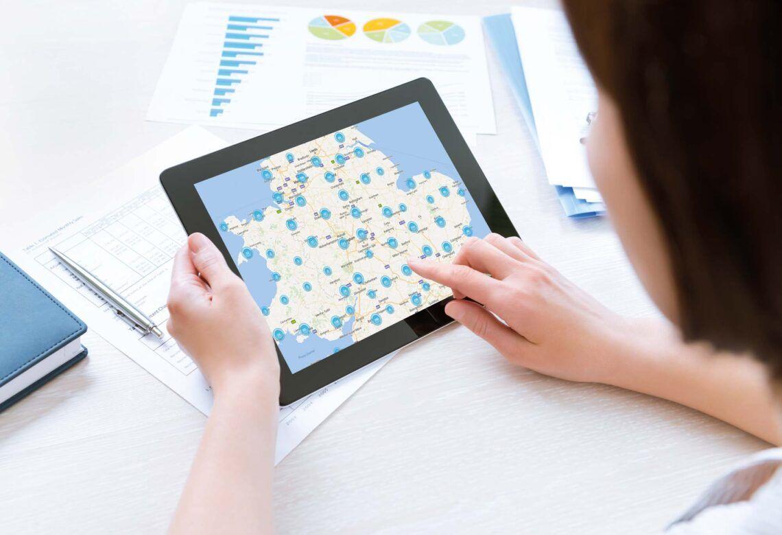 A person checks a map of fuel stations on a tablet beside printed charts