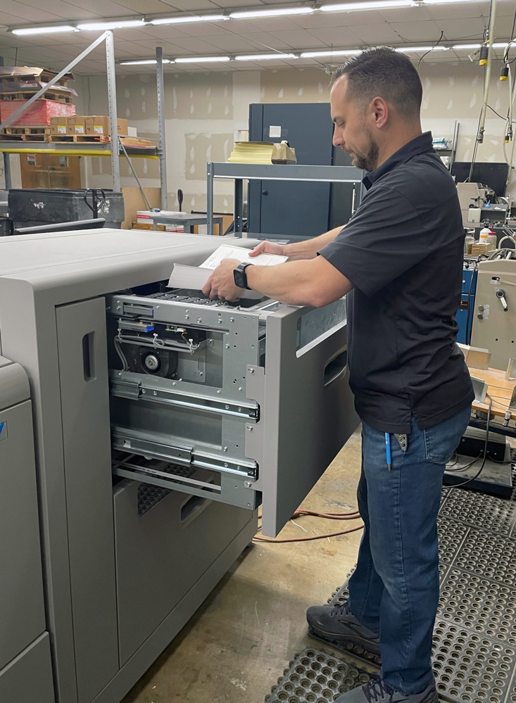 A WhiteOak production worker feeds printed sheets into a Morgana booklet maker